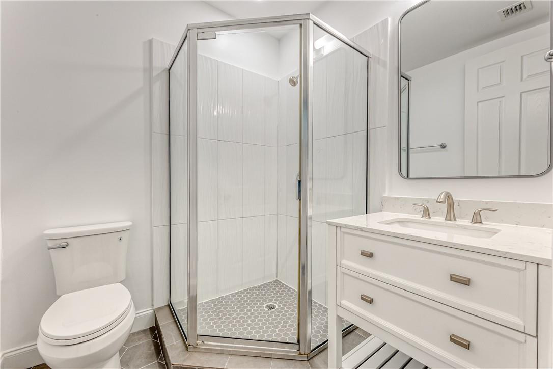 Bathroom with a glass corner shower, white vanity, and toilet.