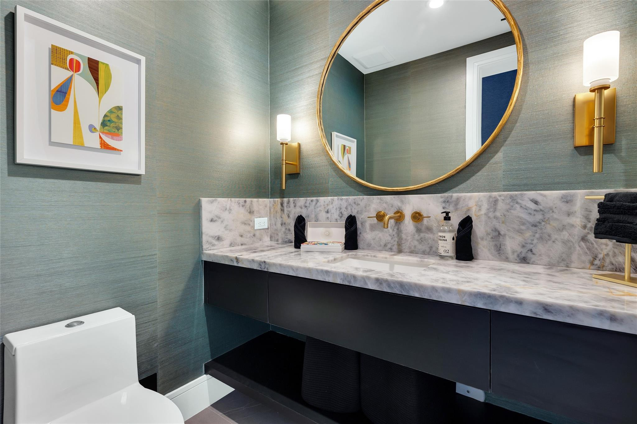 Bathroom with a marble vanity, brass fixtures, round gold-framed mirror, and teal textured walls.