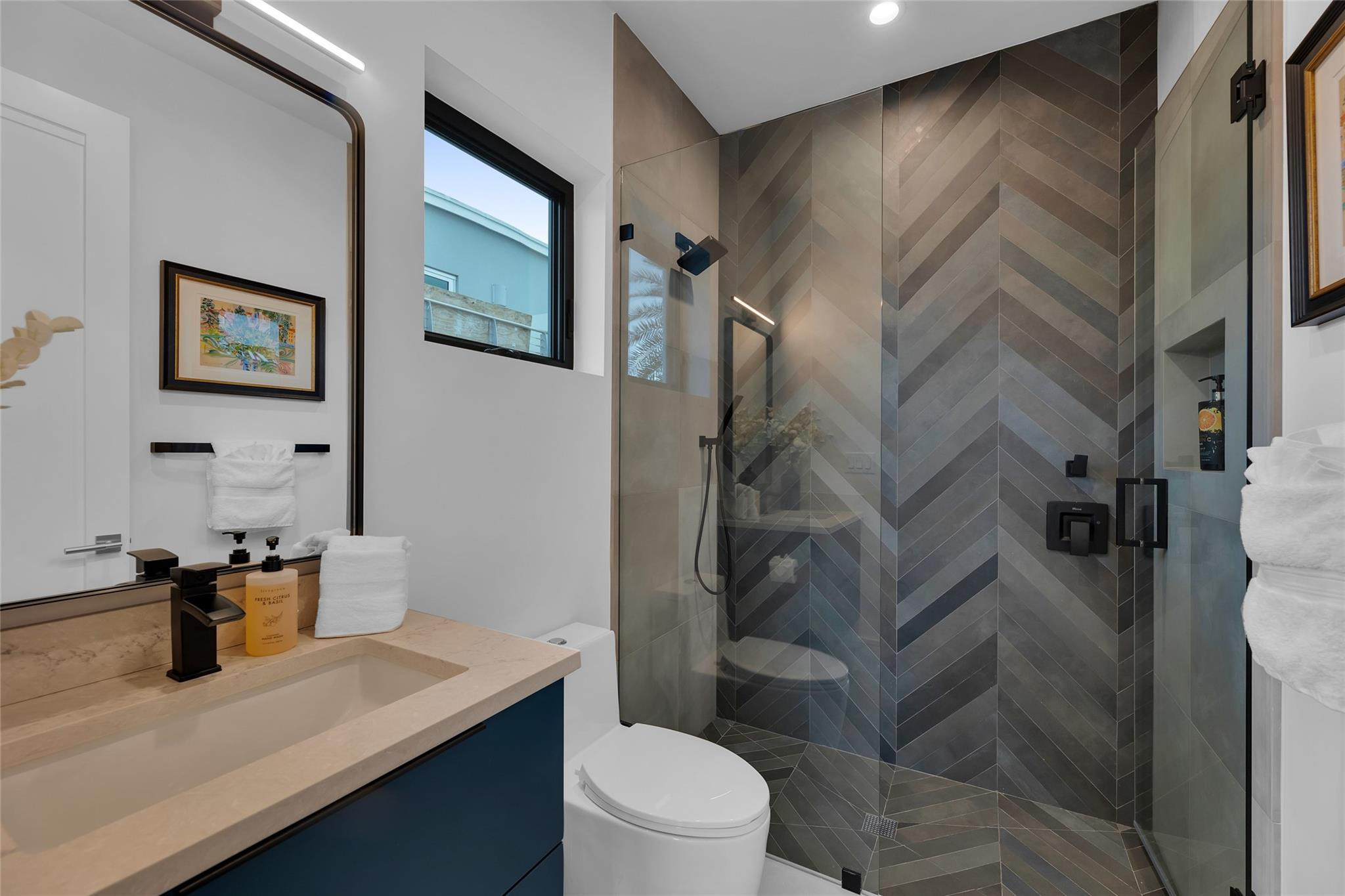 Modern bathroom with a glass shower, dark chevron tile, and a stone vanity countertop.