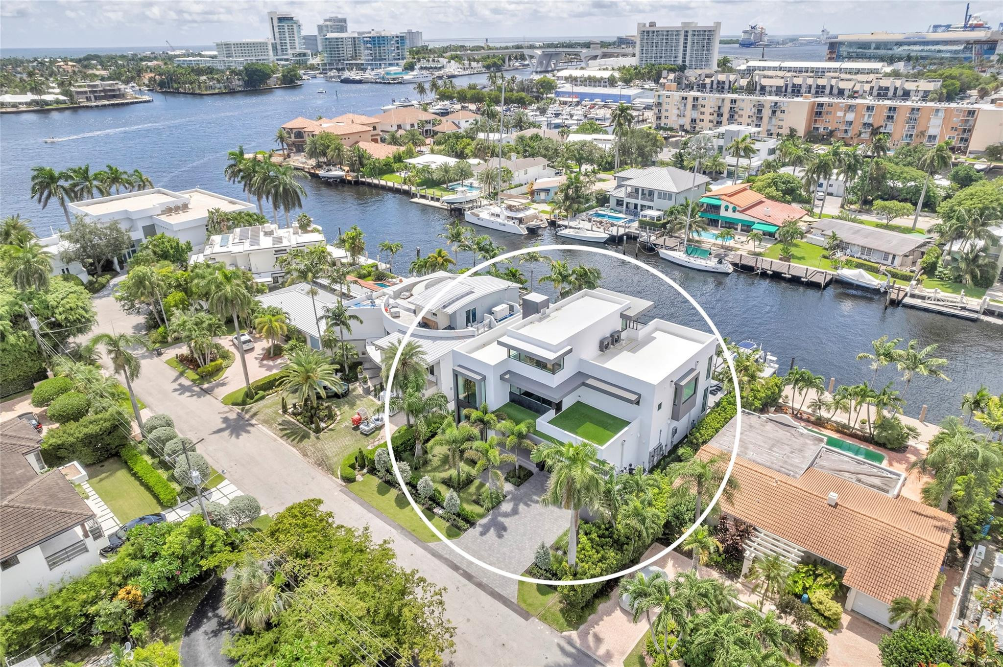 Aerial view of a modern white home circled beside a canal in a palm-lined neighborhood.