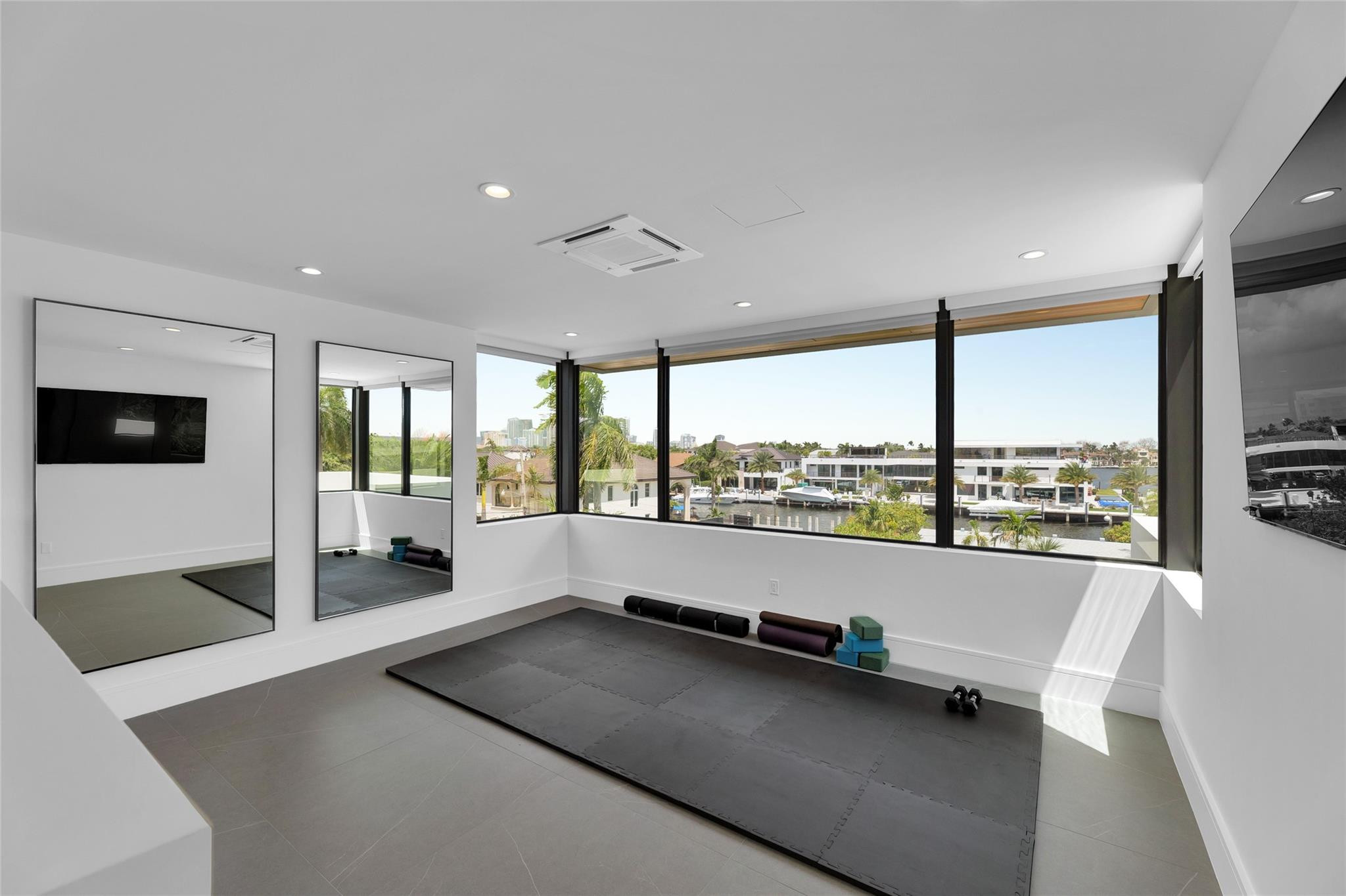 Bright home gym with mirrored walls, workout equipment, and wide windows overlooking a canal.