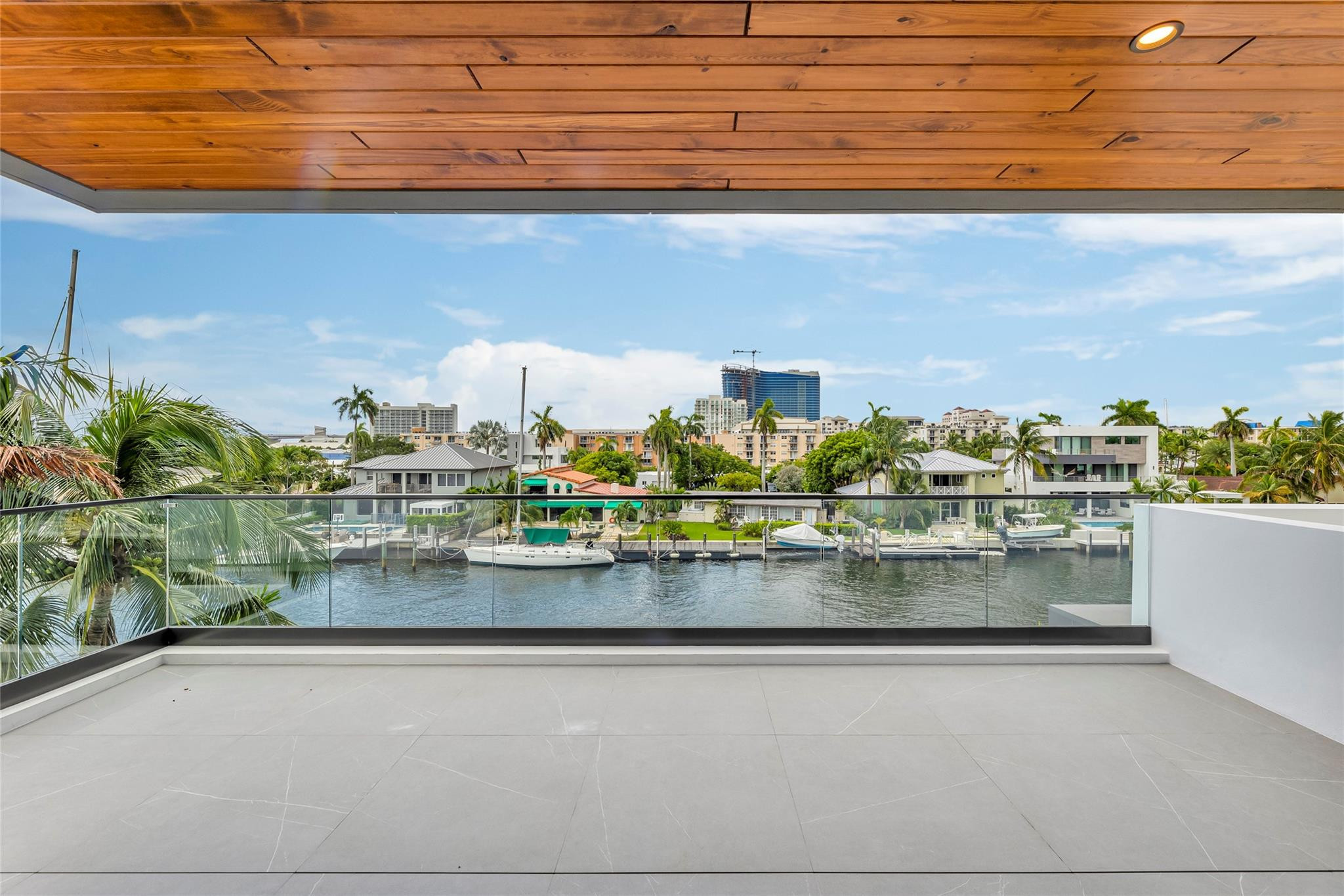 Covered balcony overlooking a boat-lined canal, palm trees, and the city skyline.