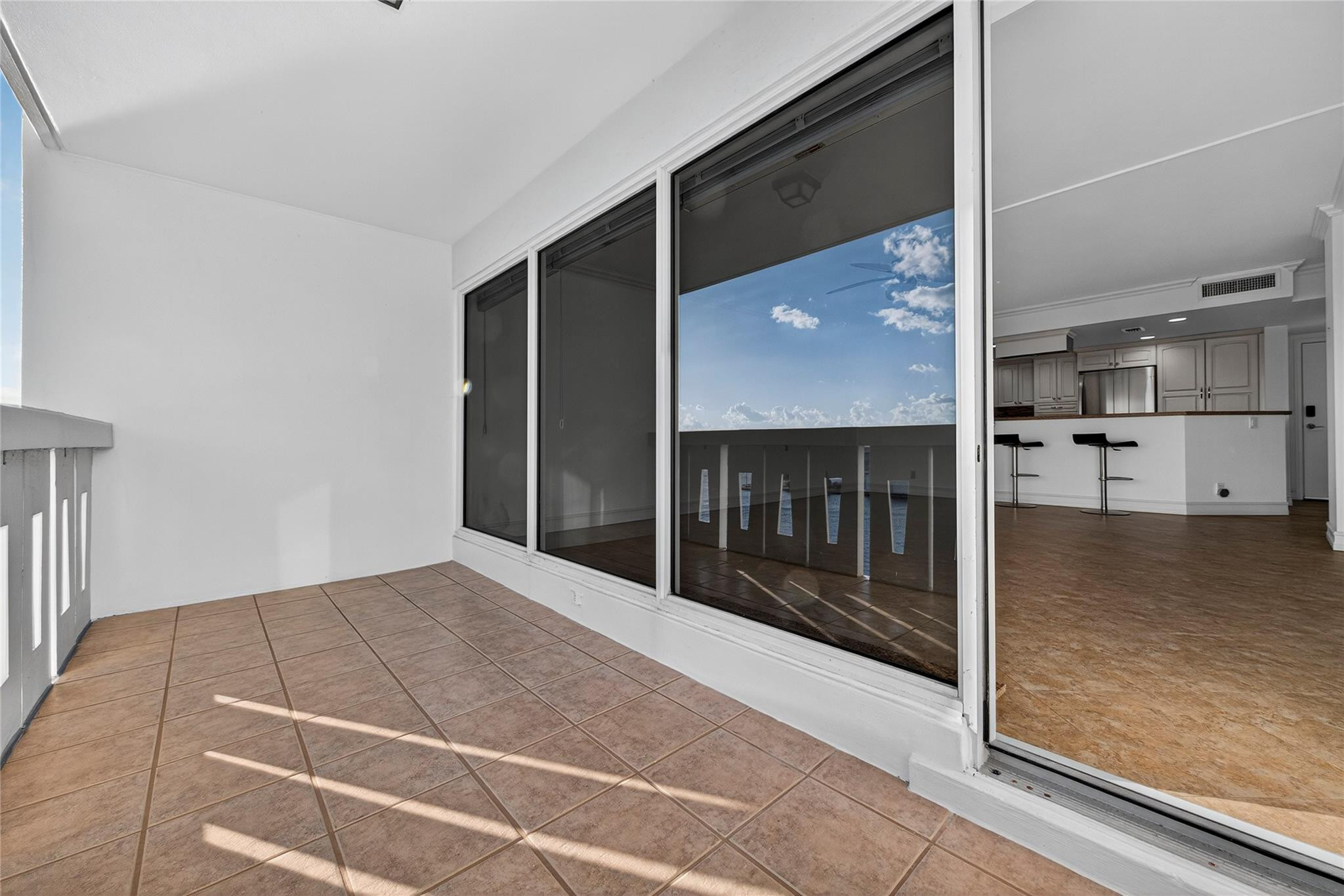 Tiled apartment balcony overlooking the water, with sliding glass doors opening to a kitchen.