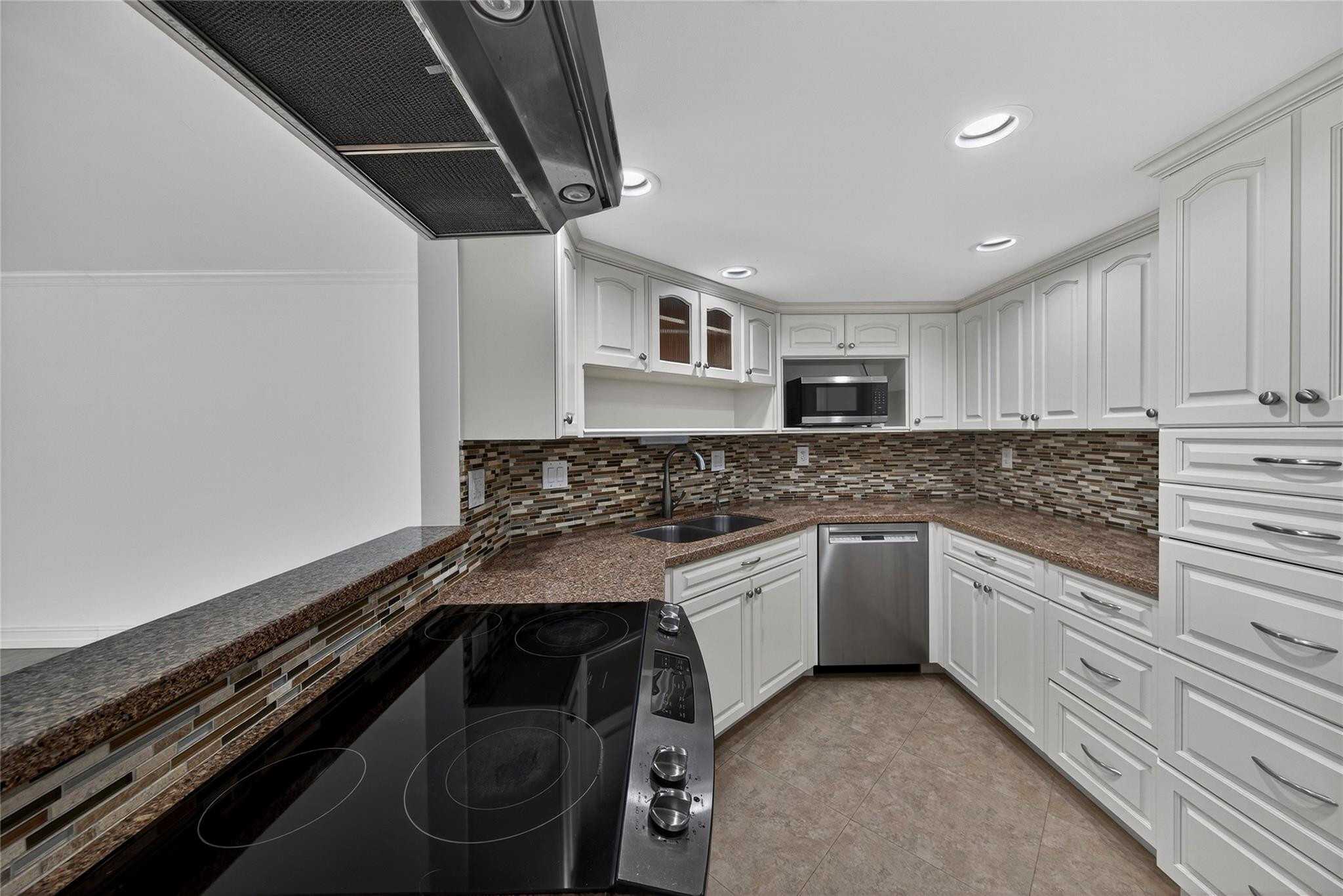 Kitchen with white cabinets, granite counters, mosaic backsplash, black cooktop, and stainless steel dishwasher.