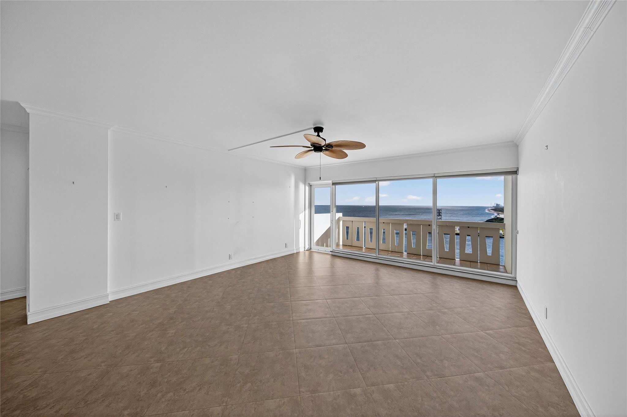 Vacant living room with tiled floors, a ceiling fan, and sliding doors overlooking the ocean.