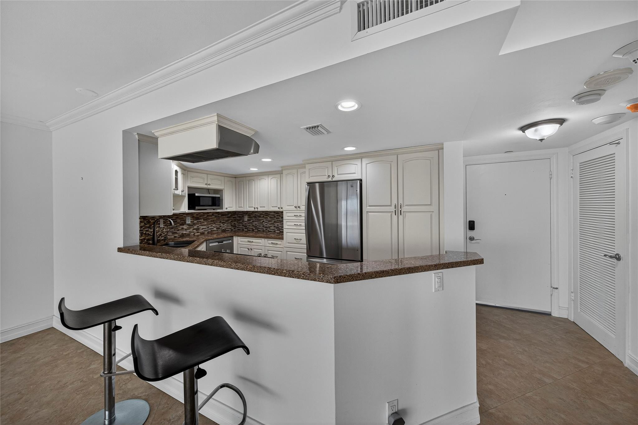 Kitchen with white cabinets, stainless steel appliances, granite breakfast bar, and black stools.