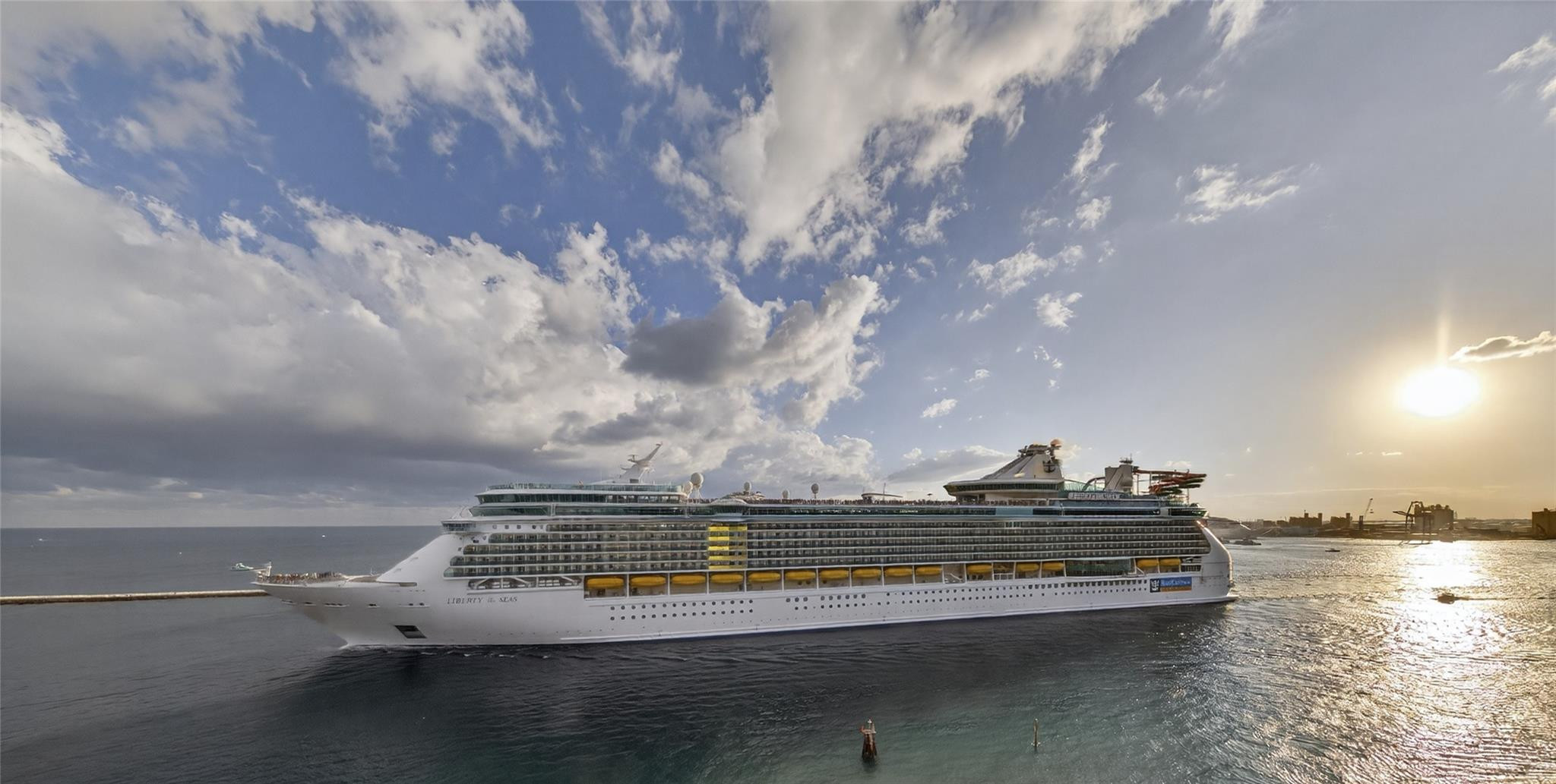 Cruise ship crossing the water at sunset beneath dramatic clouds.