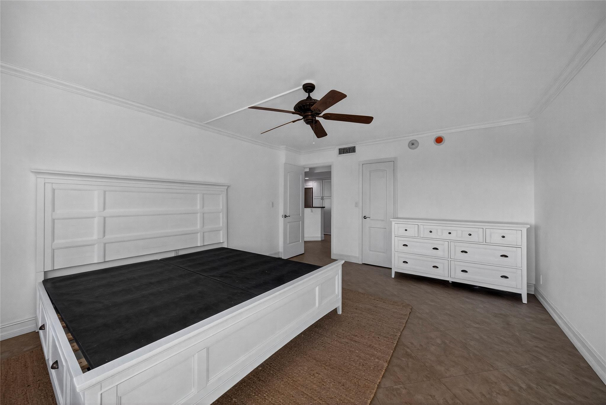 Bedroom with white paneled bed frame, matching dresser, ceiling fan, and brown tile flooring.