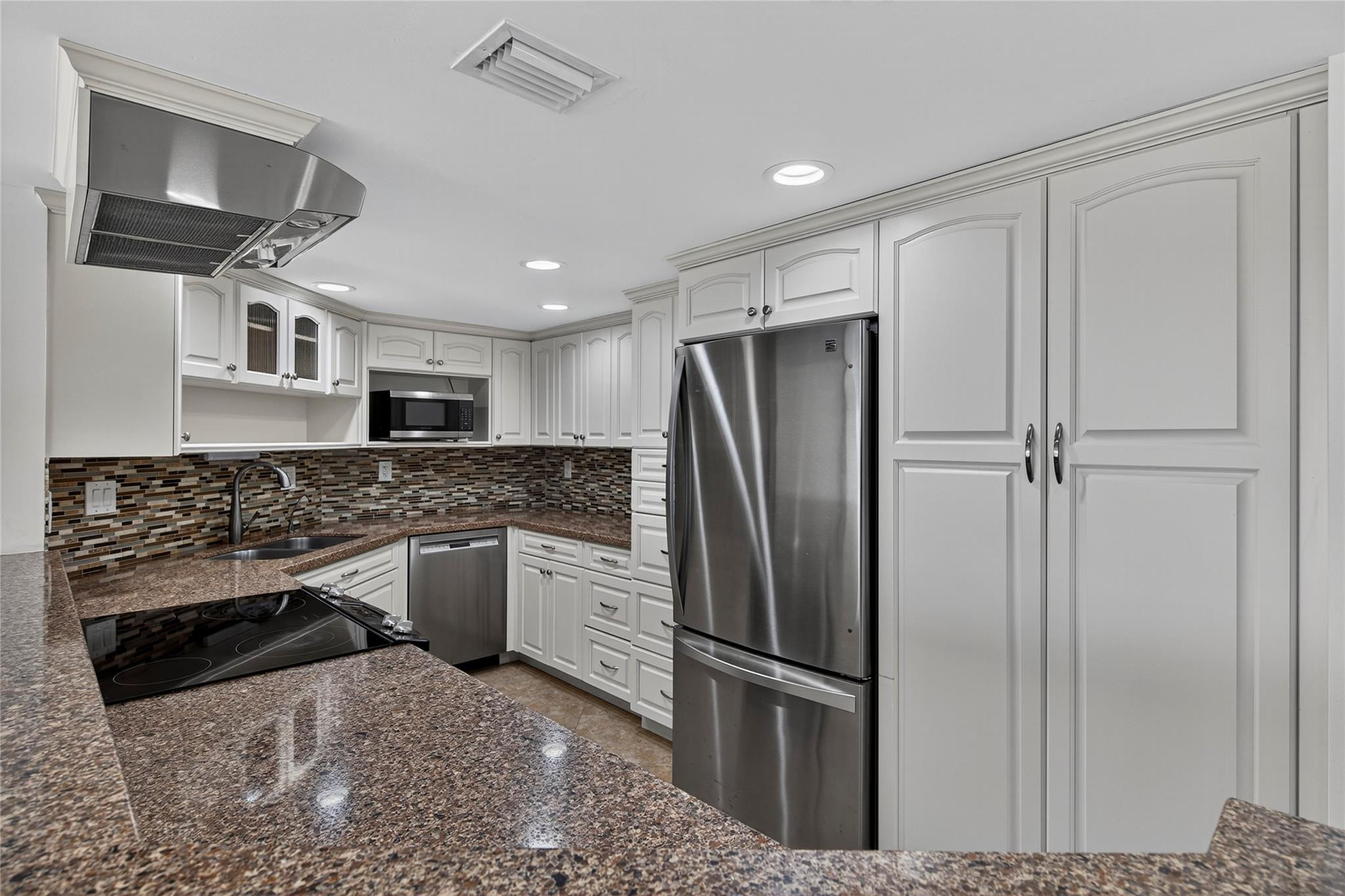 Kitchen with white cabinets, stainless steel appliances, granite counters, and a multicolored tile backsplash.