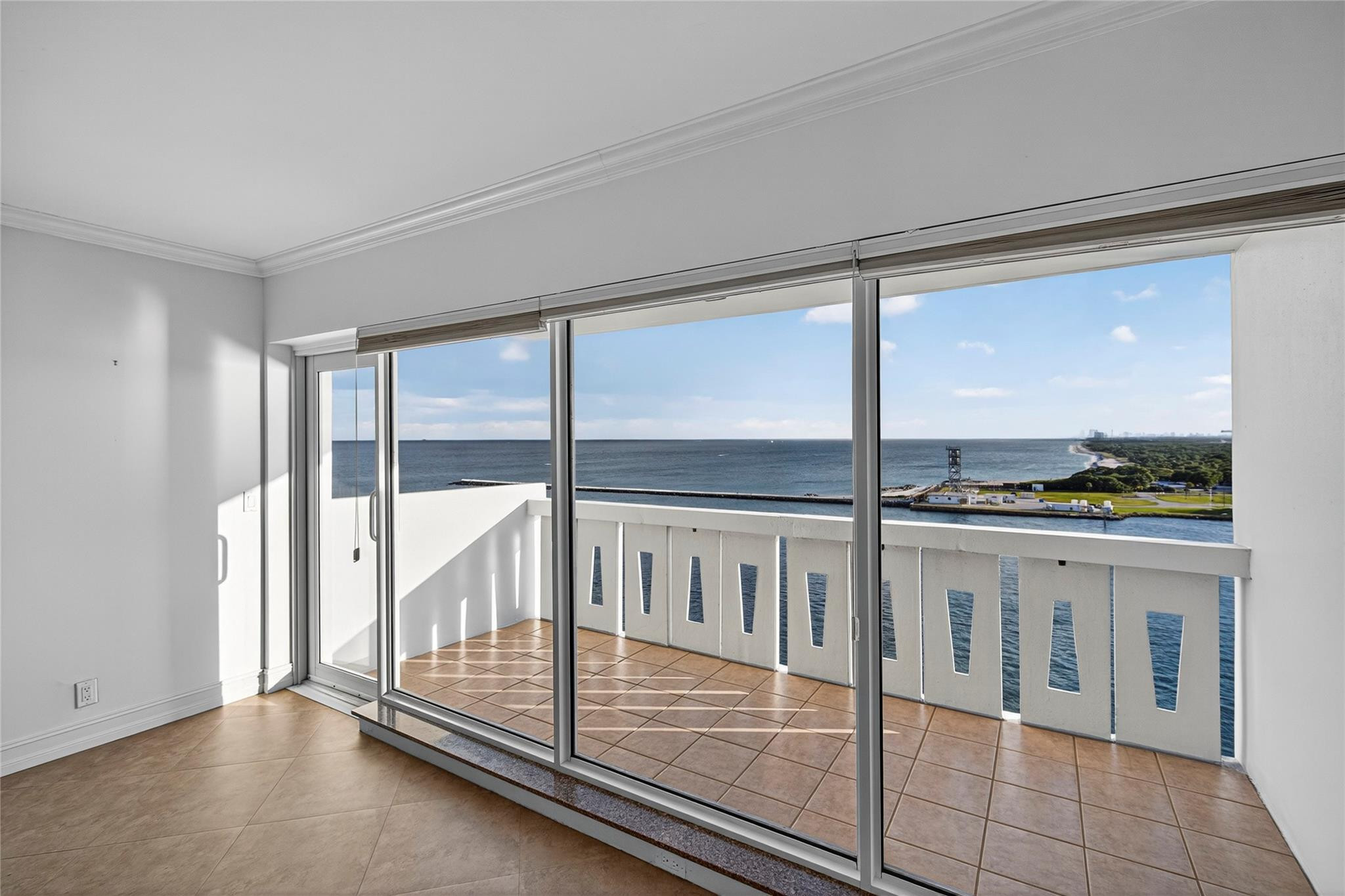 Empty tiled room with sliding glass doors opening to an ocean-view balcony.