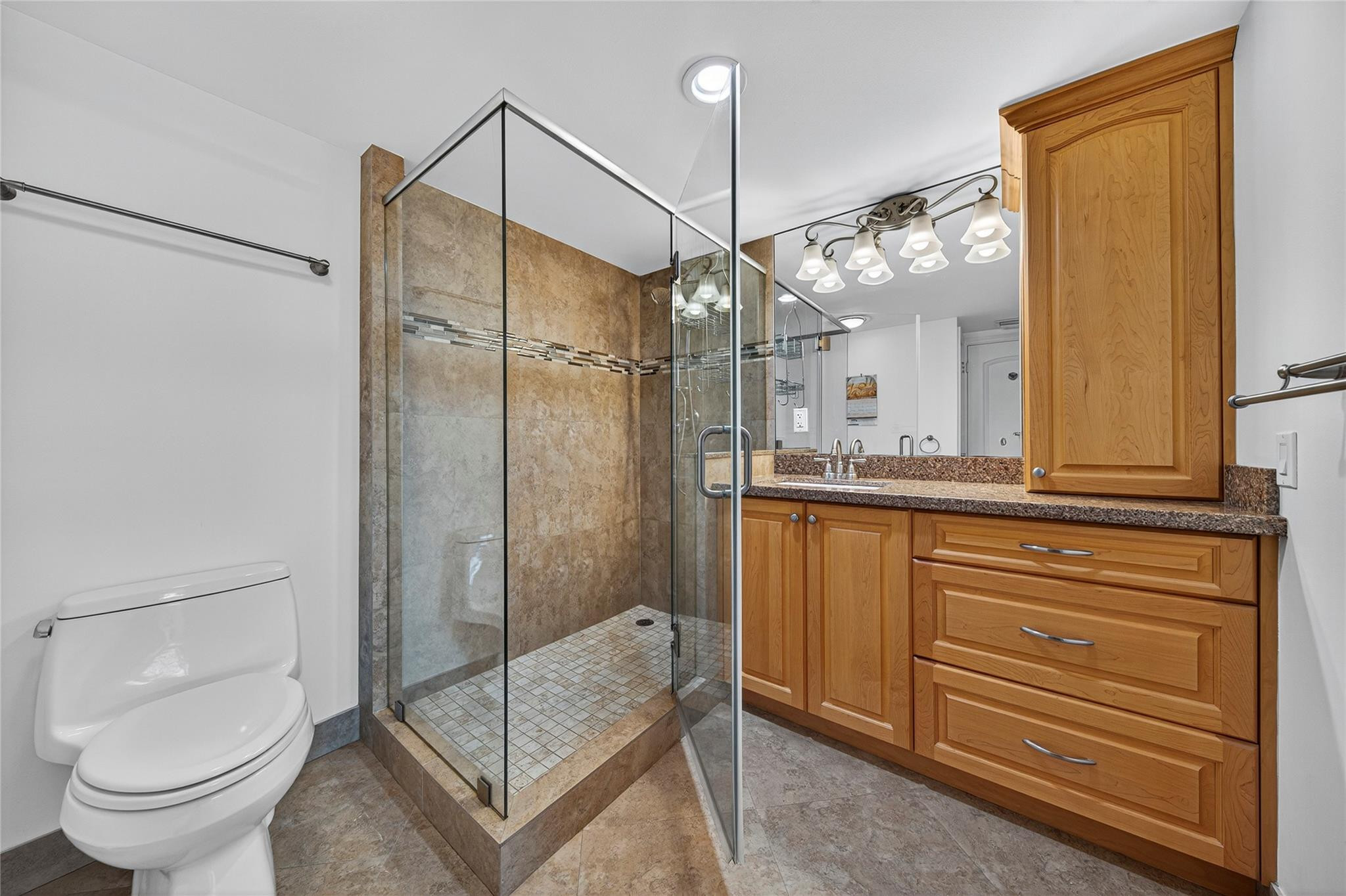 Bathroom with a glass walk-in shower, tan stone tile, and a wood vanity with granite countertop.