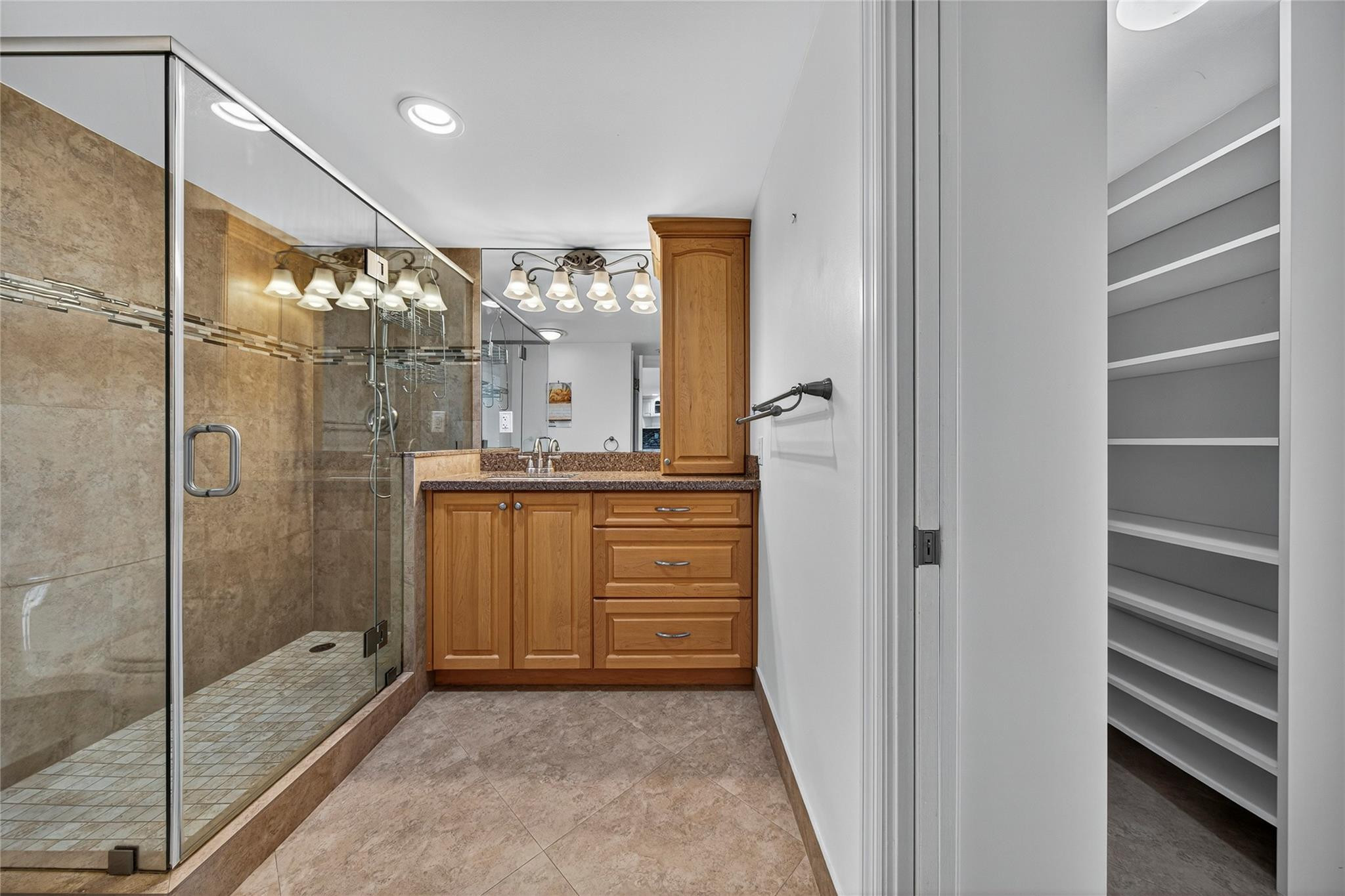 Bathroom with a glass walk-in shower, wood vanity, and open shelving beyond the doorway.