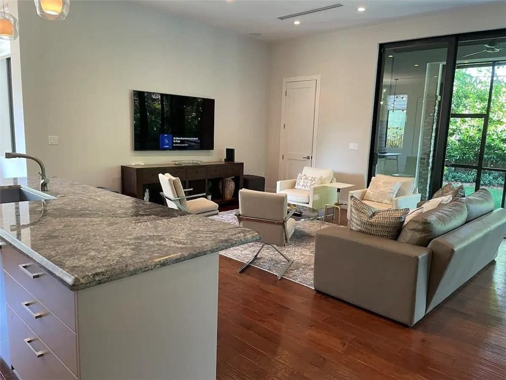 Open-plan living room with a granite kitchen island, hardwood floors, and sliding glass doors to greenery.