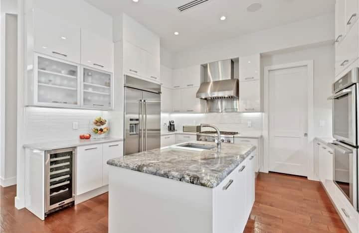 Bright white kitchen with a large stone island, stainless steel appliances, and warm wood floors.