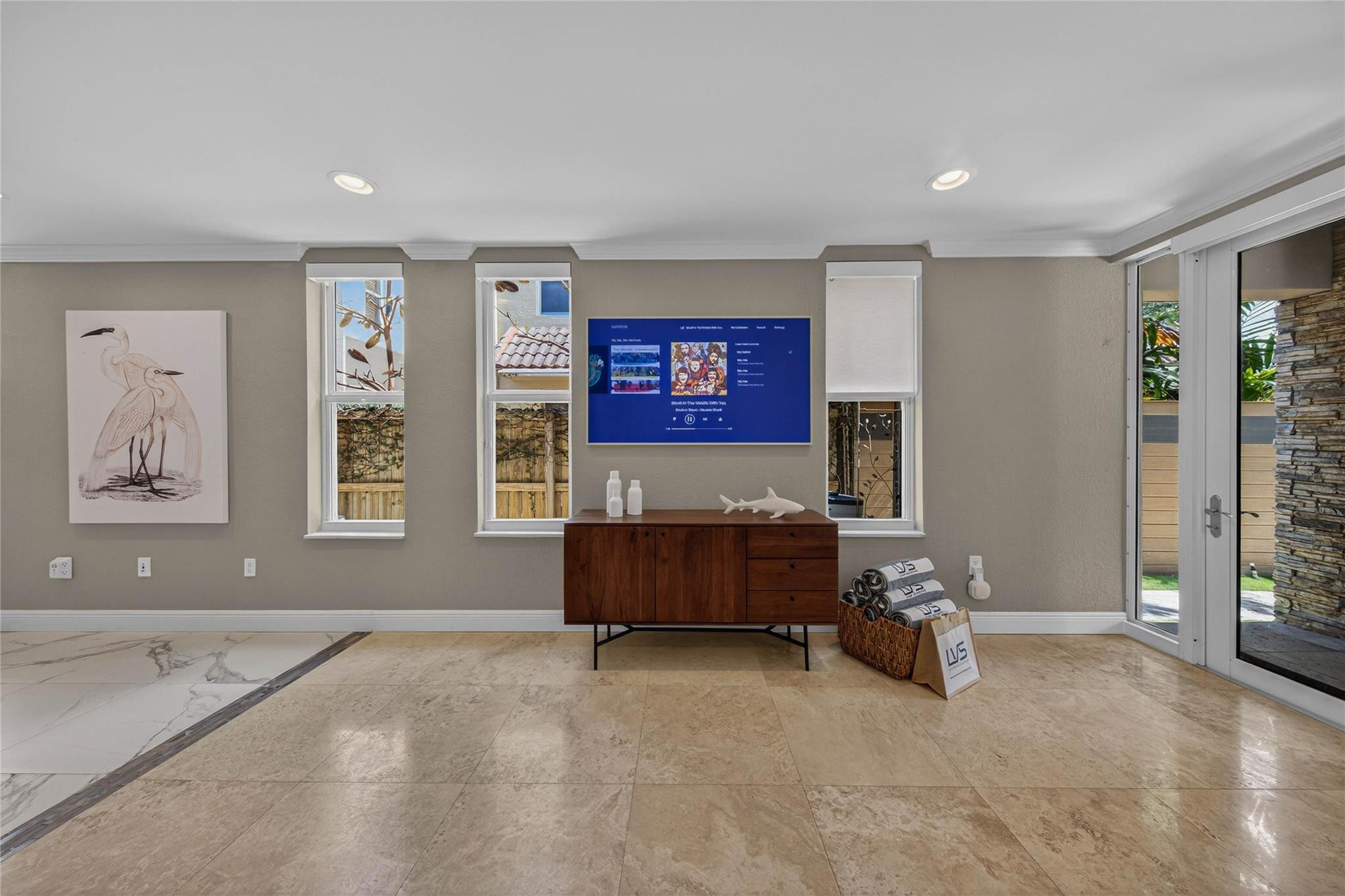 Furnished room with stone tile floors, a wood console, wall-mounted television, and glass patio doors.