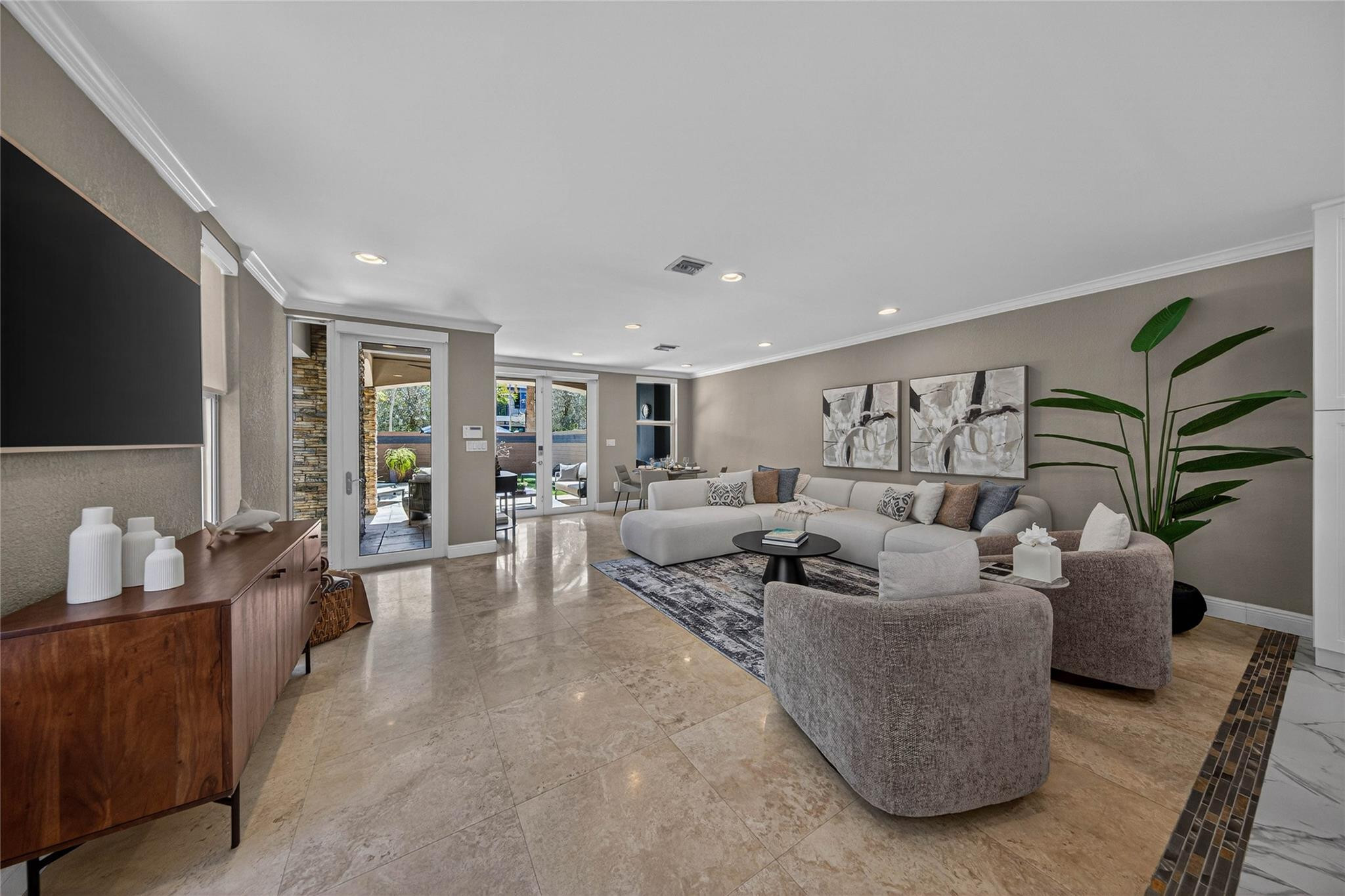 Staged living room with a gray sectional, patterned rug, glossy stone floors, and glass doors to a patio.