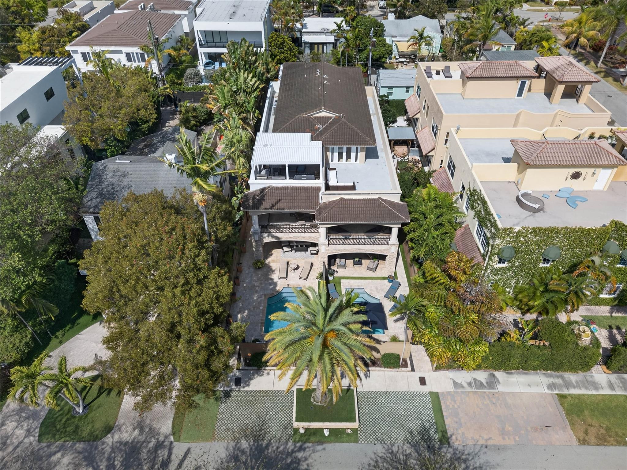 Aerial view of a two-story home with a swimming pool and palm-lined patio.