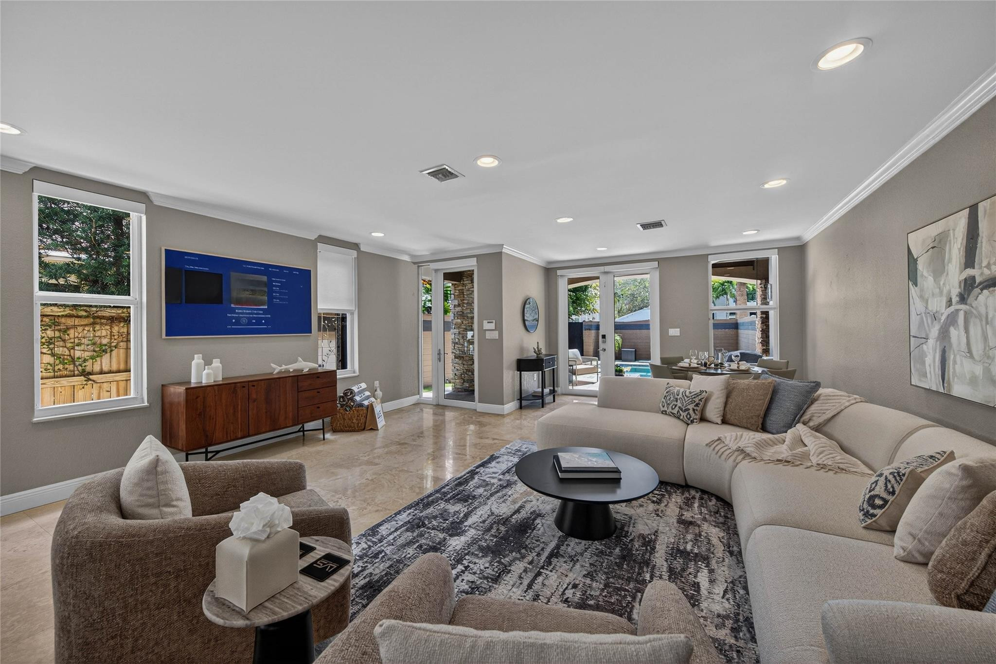 Staged living room with a curved cream sectional, patterned rug, and sliding doors overlooking a pool.