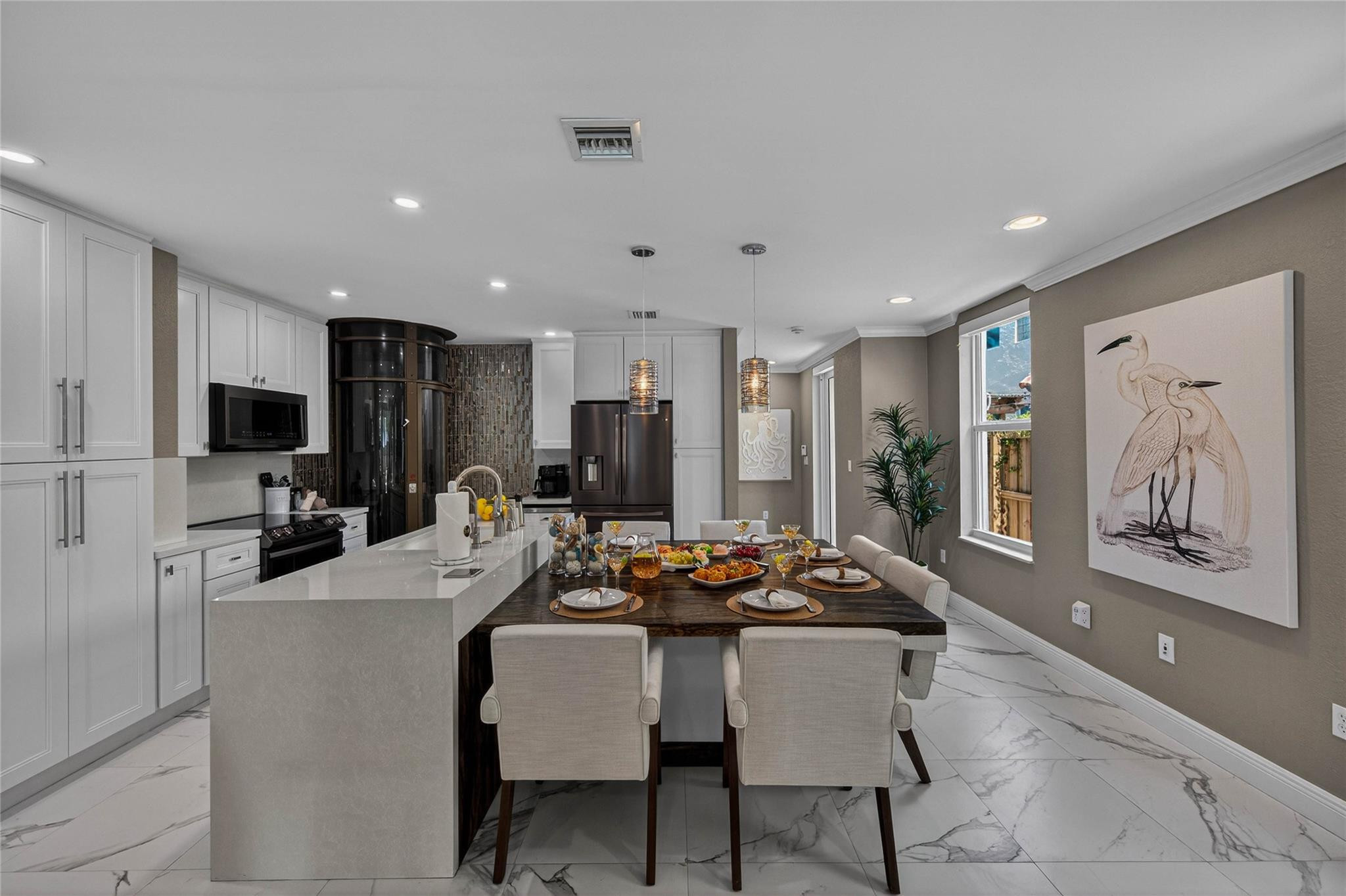 Staged kitchen and dining area with a large stone island, set dining table, and bird artwork.