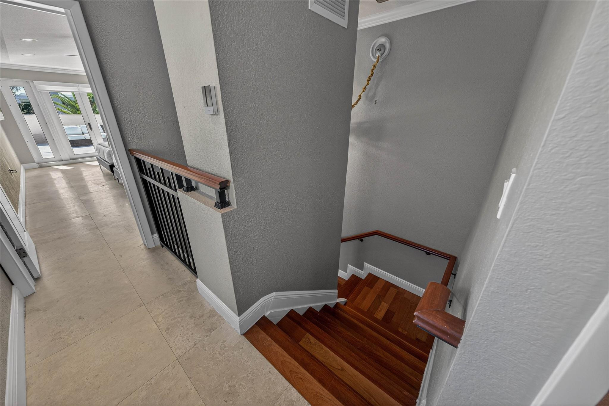 Tiled hallway beside a descending hardwood staircase with wood handrails and glass doors beyond.