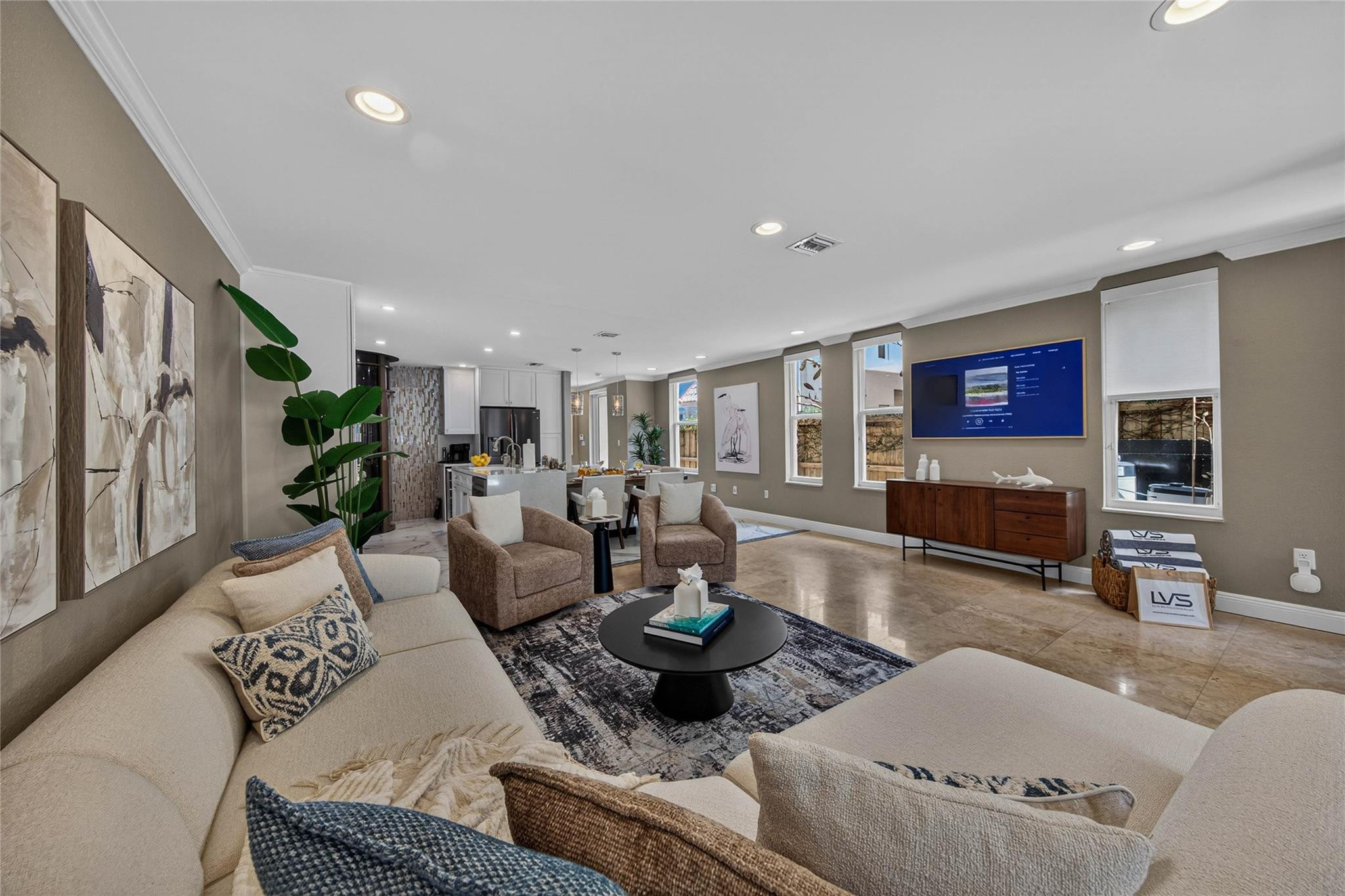 Staged living room with cream sofas, a round coffee table, and an open kitchen beyond.