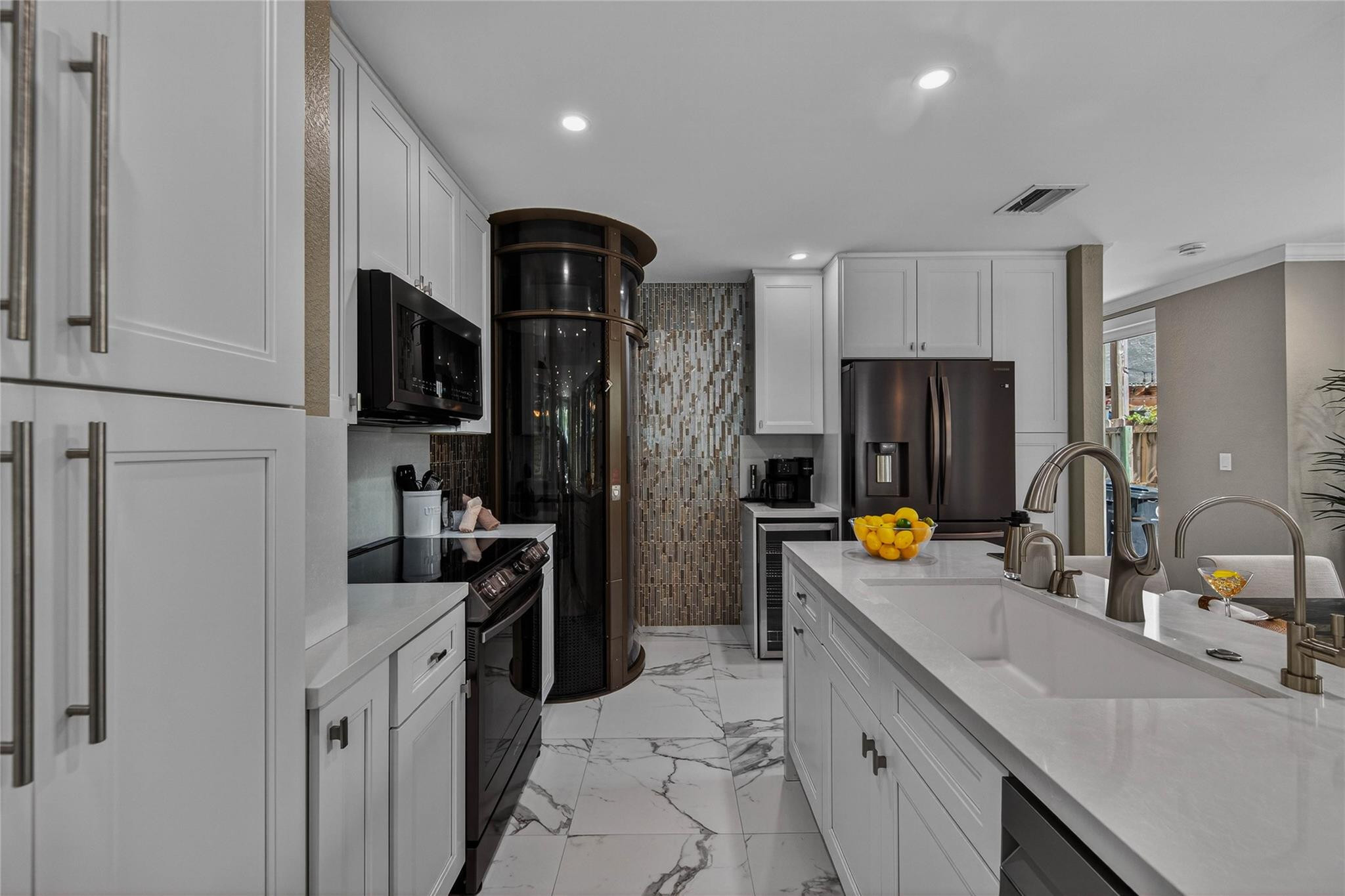 Modern white kitchen with a large island and curved glass wine cellar.