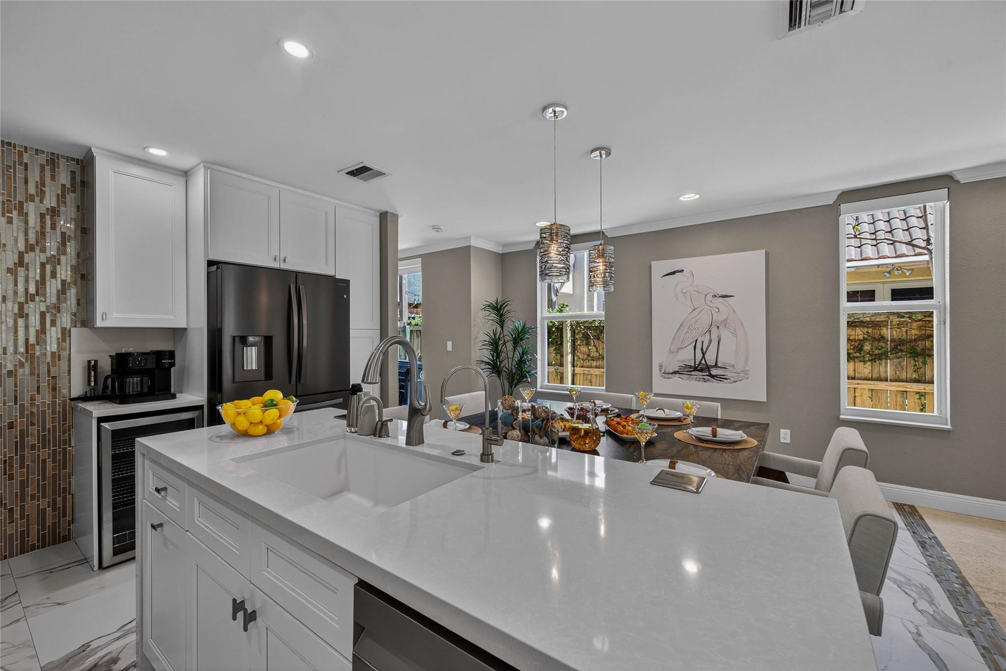 Kitchen with a large white island and sink, stainless steel refrigerator, and dining table set beneath pendant lights.