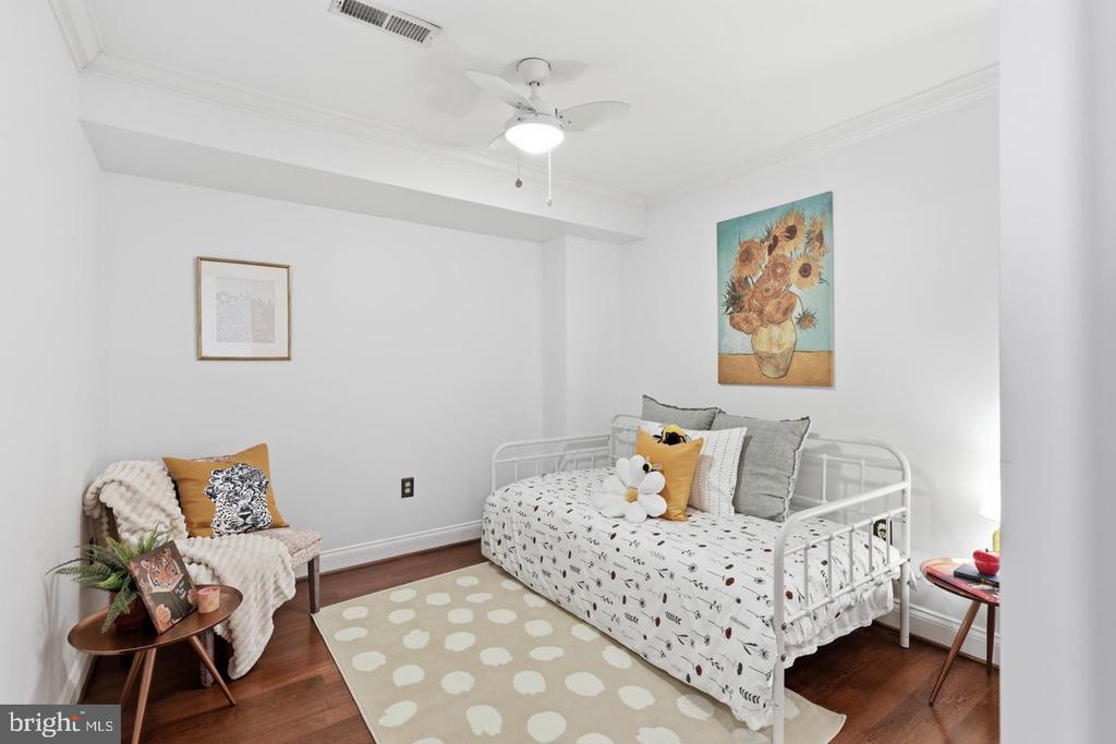 Staged bedroom with a white daybed, sunflower painting, cozy chair, and spotted rug.