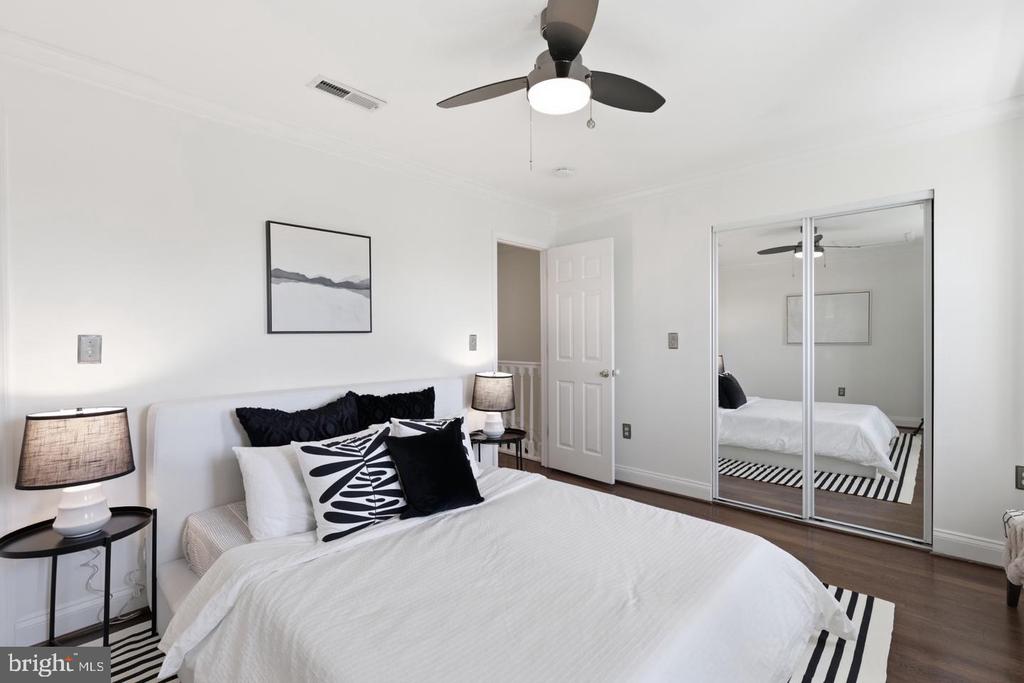 Staged bedroom with a white bed, black-and-white pillows, and mirrored closet doors.