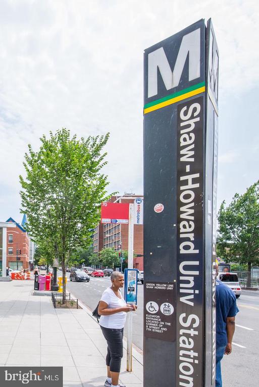 Shaw-Howard University Metro station sign beside a city sidewalk and leafy trees.