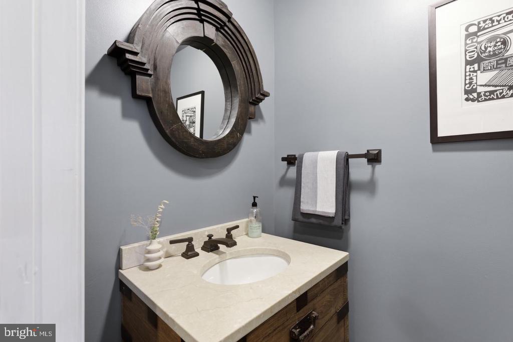Bathroom vanity with a cream countertop, dark wood cabinetry, and a large arched mirror.