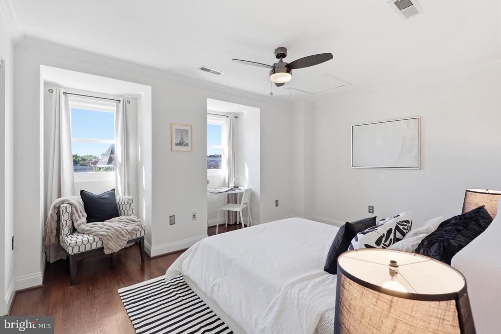 Bedroom with a white bed, dark wood floors, two windows, and a small sitting area.