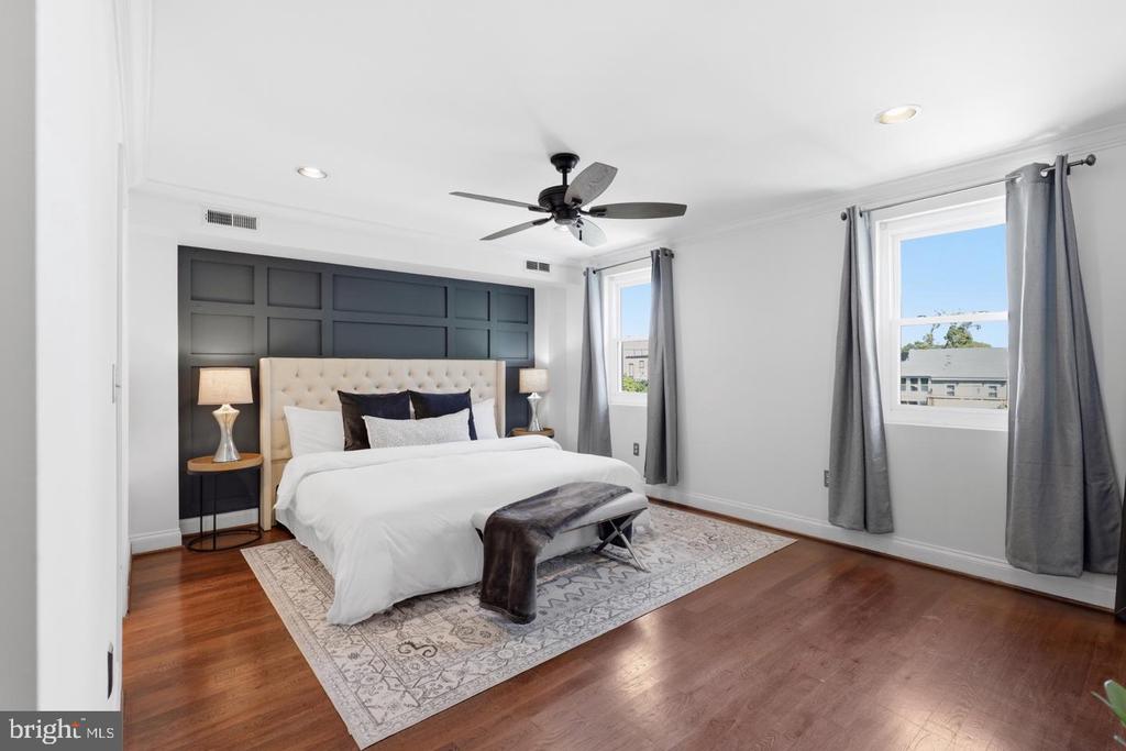 Bedroom with a white upholstered bed, dark paneled accent wall, and two curtained windows.