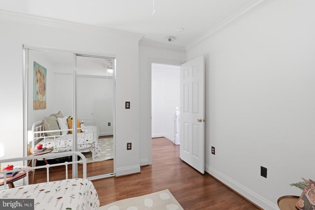 Bedroom with mirrored closet doors, hardwood floors, and an open doorway.