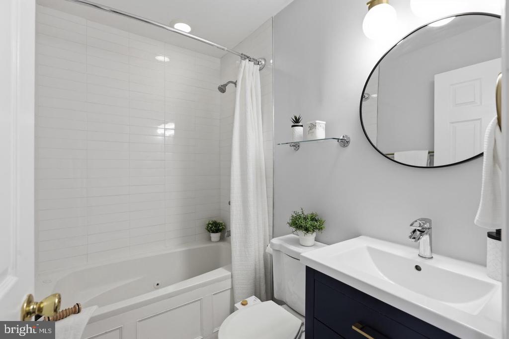 Bathroom with a white tiled tub and shower, oval mirror, and navy vanity.