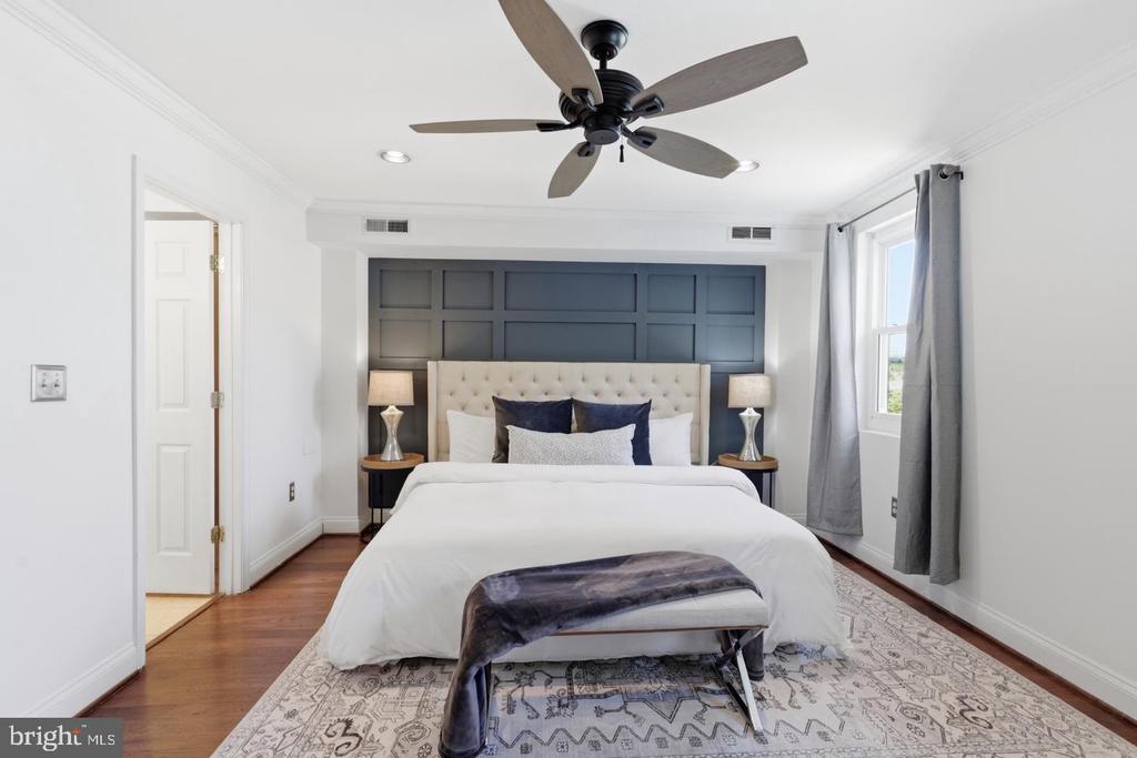 Staged bedroom with a white bed, dark blue paneled accent wall, and ceiling fan.