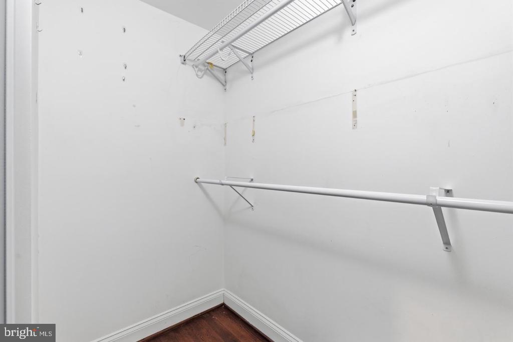 Empty walk-in closet with wire shelving, a long hanging rod, and dark hardwood flooring.