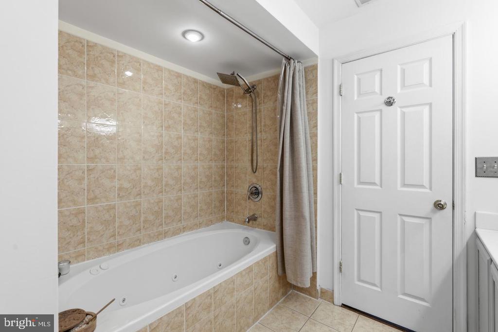 Bathroom with a jetted bathtub, beige tile, and a shower curtain.