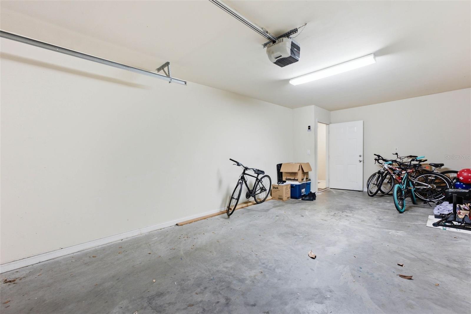 Garage with a concrete floor, overhead opener, and bicycles and boxes stored near the open door.