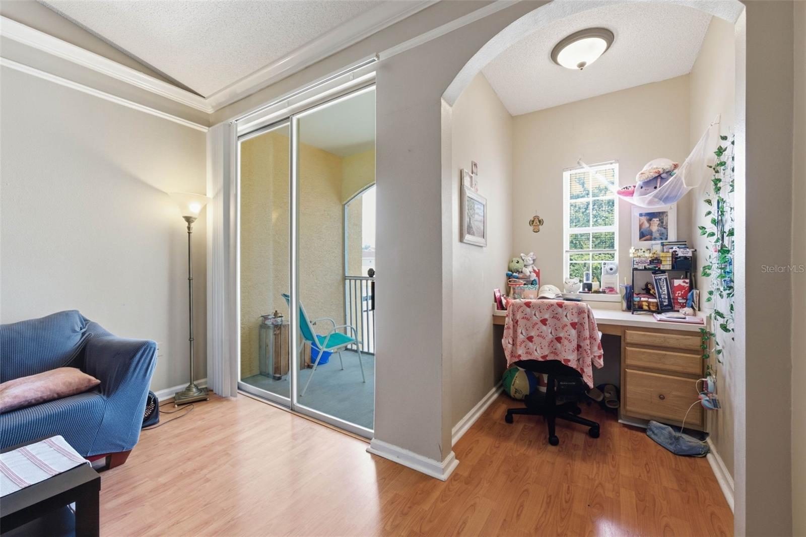 Furnished room with a blue armchair, balcony doors, and a desk tucked beneath a window.