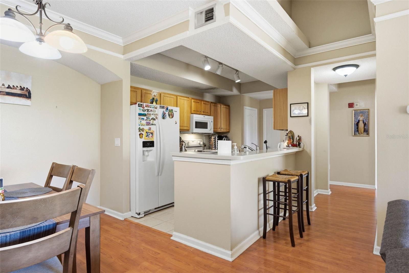 Kitchen with a breakfast bar, light wood cabinets, white appliances, and adjoining dining area.