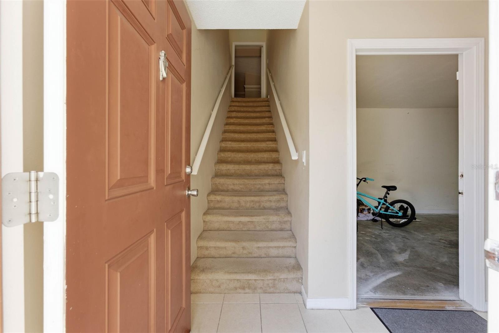 Entryway with carpeted stairs and an open garage doorway showing a turquoise bicycle.