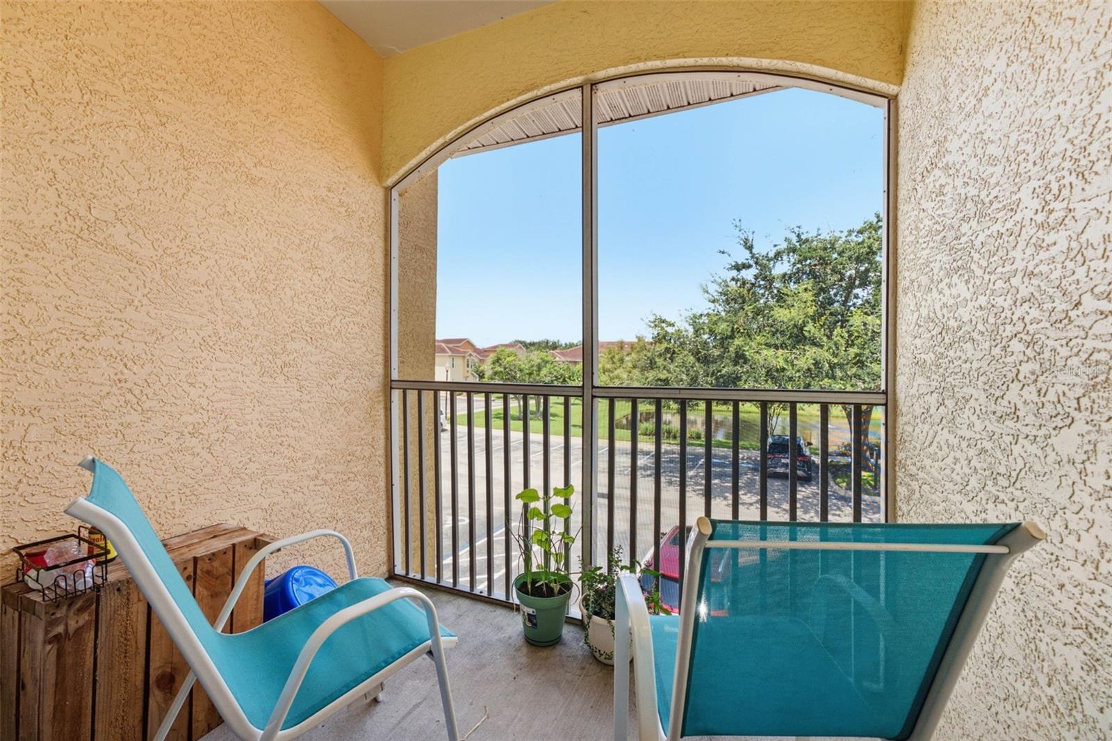 Screened balcony with turquoise lounge chairs and a view of trees and a small pond.