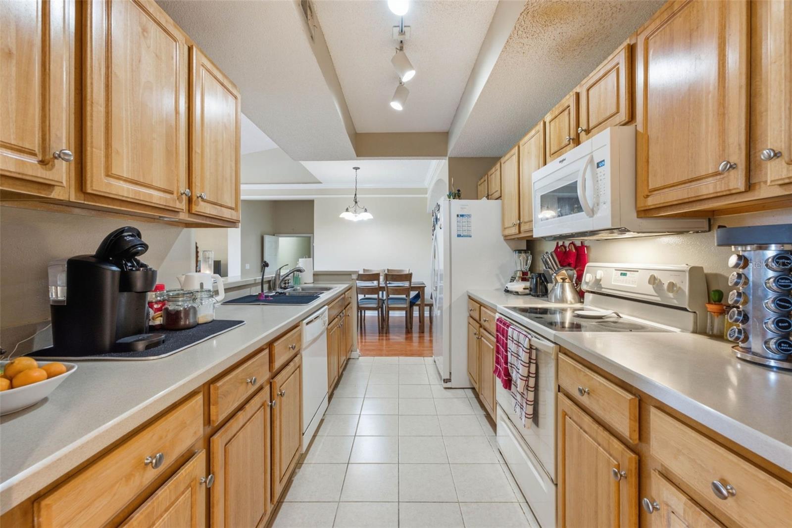 Galley kitchen with light wood cabinets, white appliances, and a dining table at the far end.