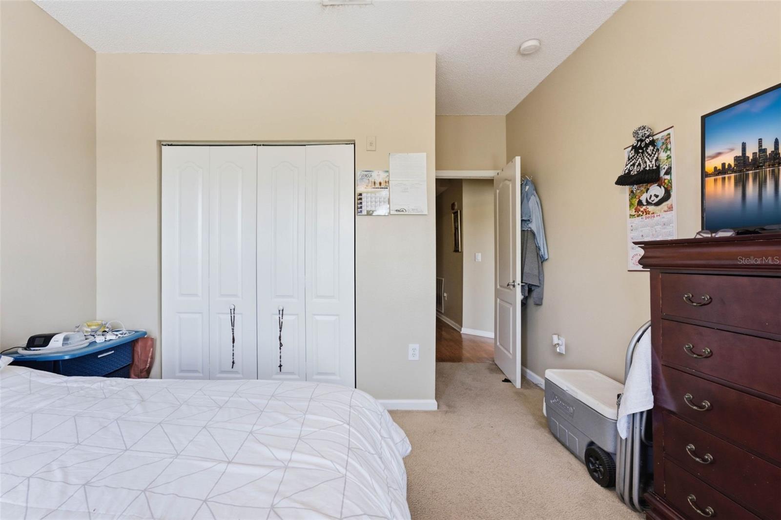 Bedroom with white closet doors, a geometric bedspread, carpet, and dark wooden dresser.