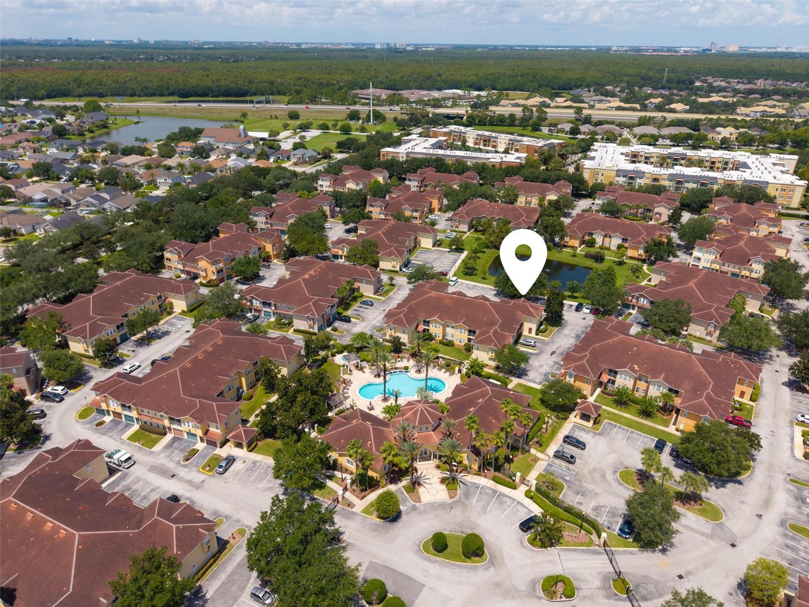 Aerial view of a residential community with a central pool and a location marker over one building.