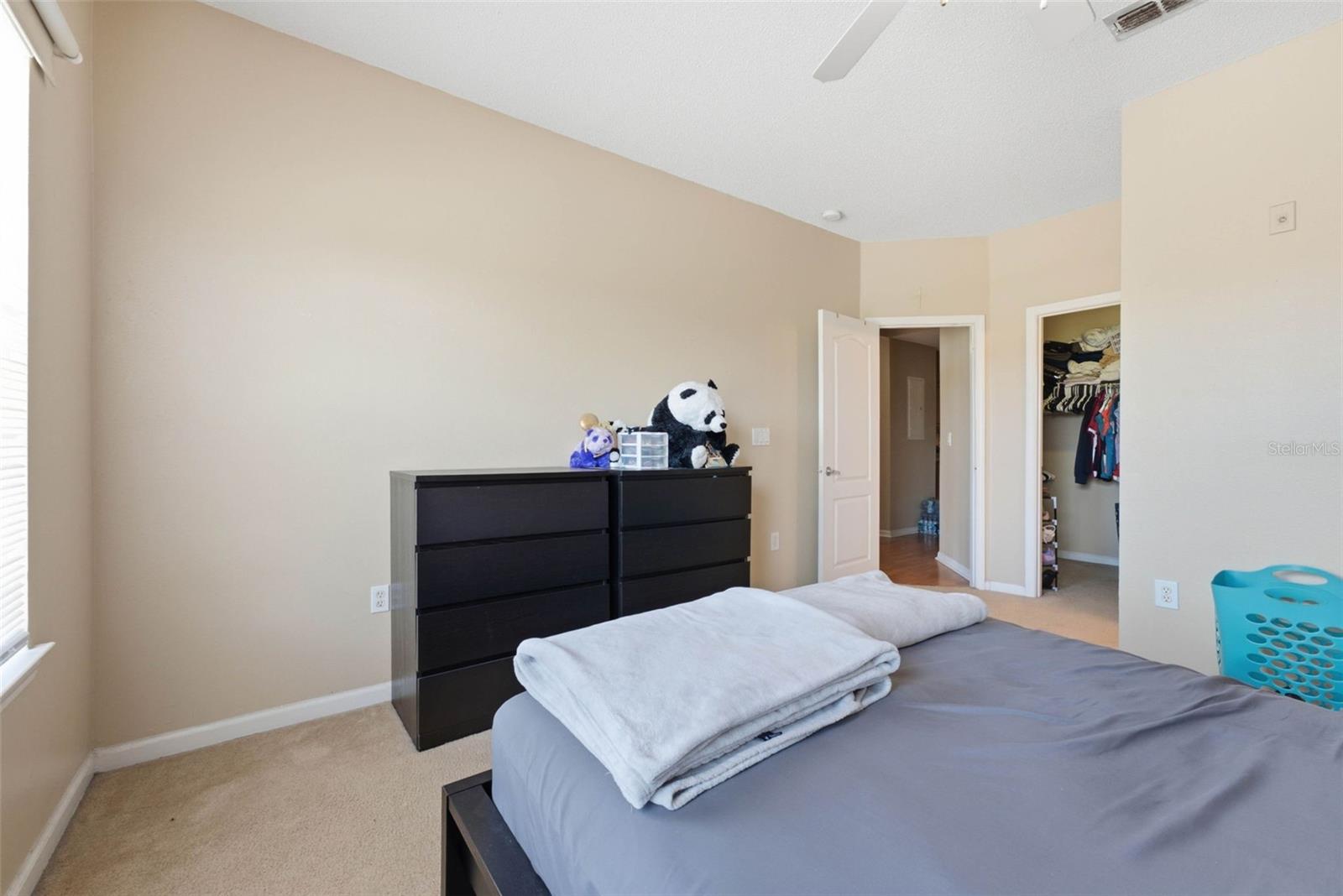 Bedroom with gray bedding, dark dressers, stuffed animals, and an open closet.