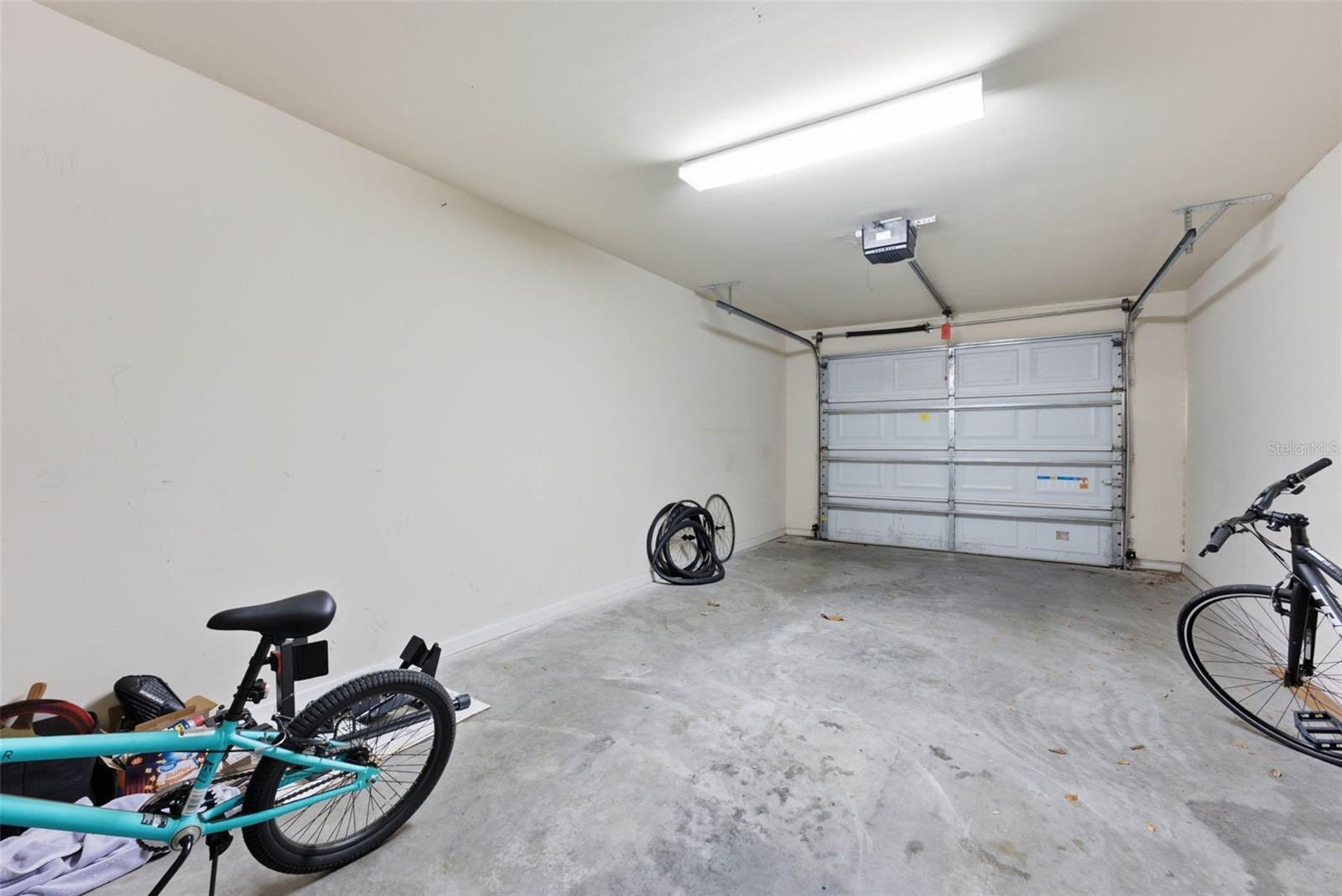 Garage with a closed sectional door, concrete floor, and bicycles along the edges.