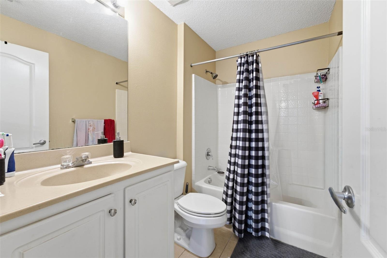 Bathroom with white vanity, toilet, and tub-shower behind a black-and-white checkered curtain.