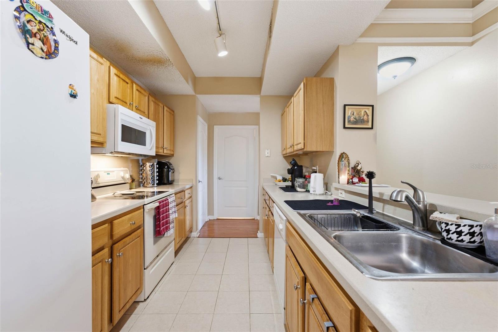 Galley kitchen with honey-colored cabinets, white appliances, tiled floor, and double-basin sink.